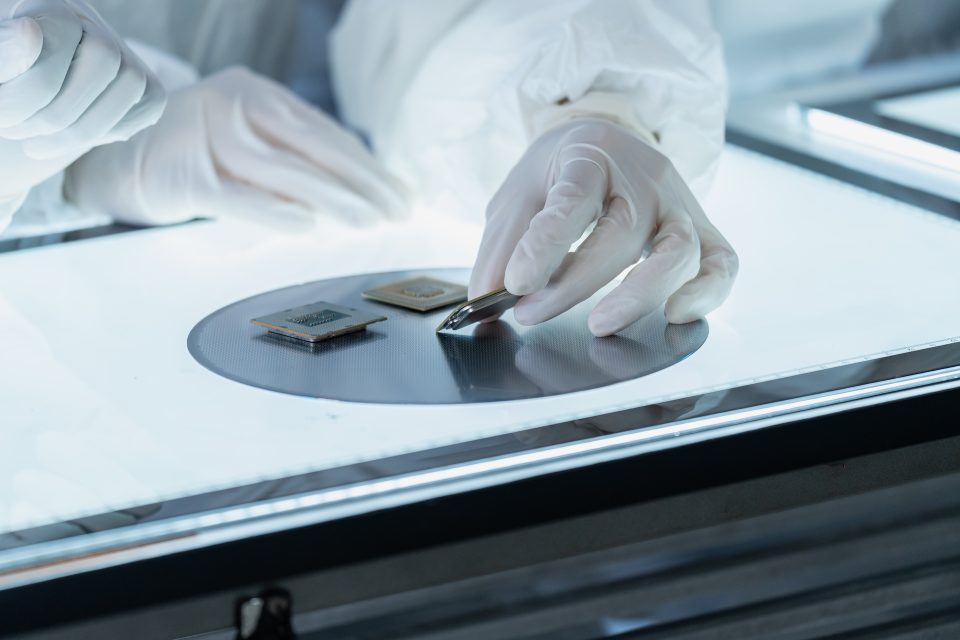 5 Engineering Factors Influencing Heat Pump Efficiency 1 Avnan | Heat Pump Efficiency | Close-up of a technician's gloved hands carefully inspecting semiconductor microchips and a silicon wafer on an illuminated light table in a cleanroom laboratory